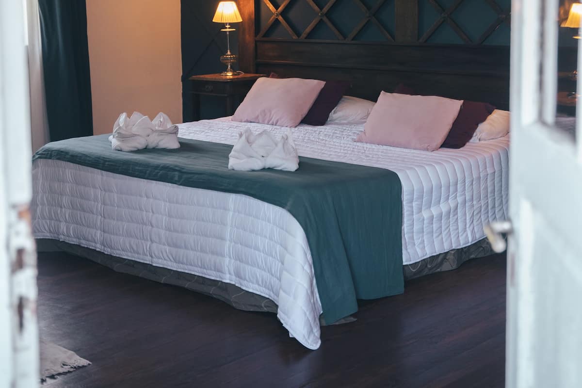 A neatly made bed with a green and white duvet, two bedside lamps, and a dark wooden headboard.