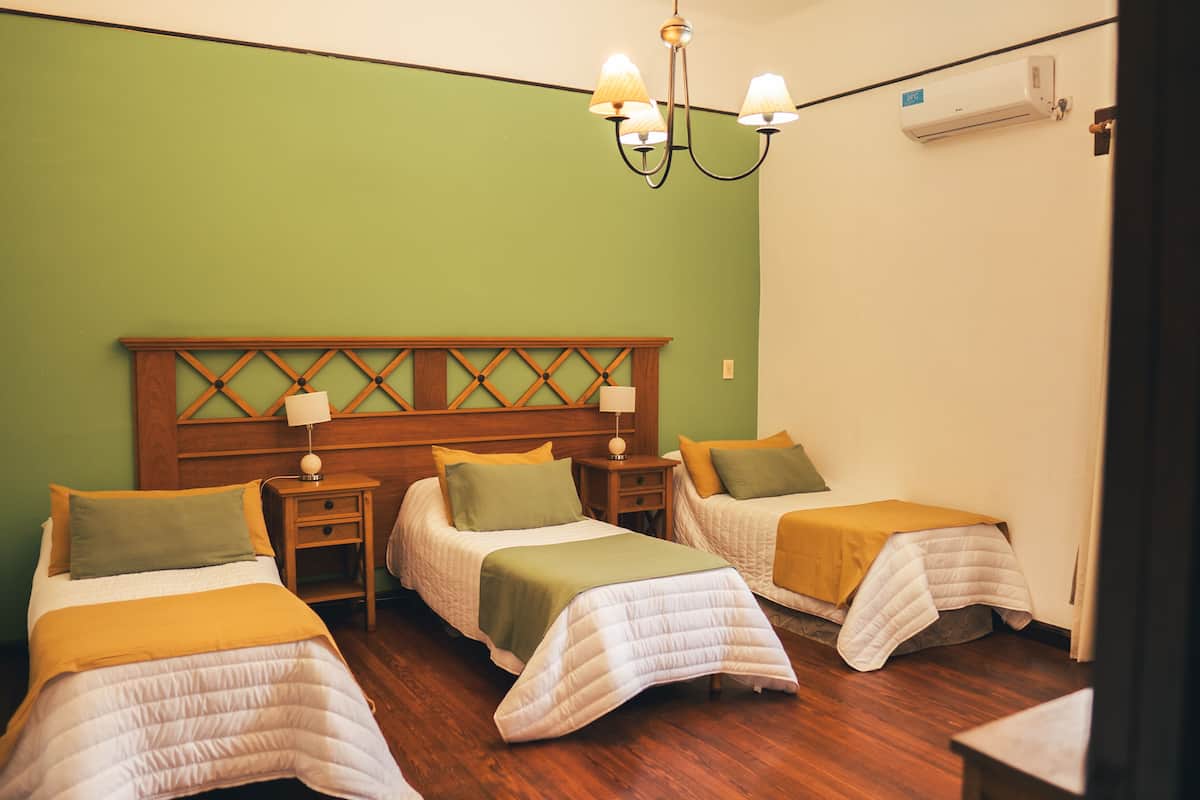 A hotel room with two beds, a wooden headboard, a nightstand, a lamp, and an air conditioning unit.