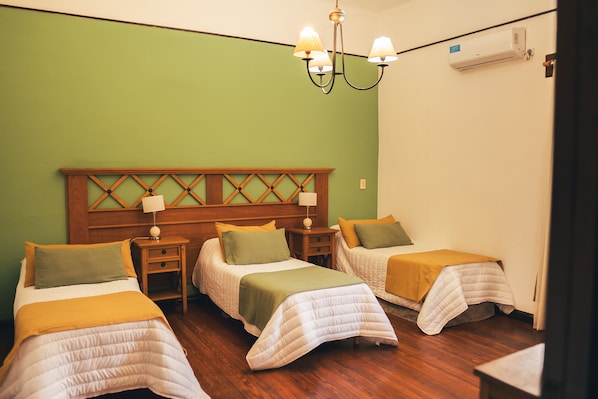 Habitación de hotel con dos camas, cabecera de madera, mesita de noche, lámpara y unidad de aire acondicionado.