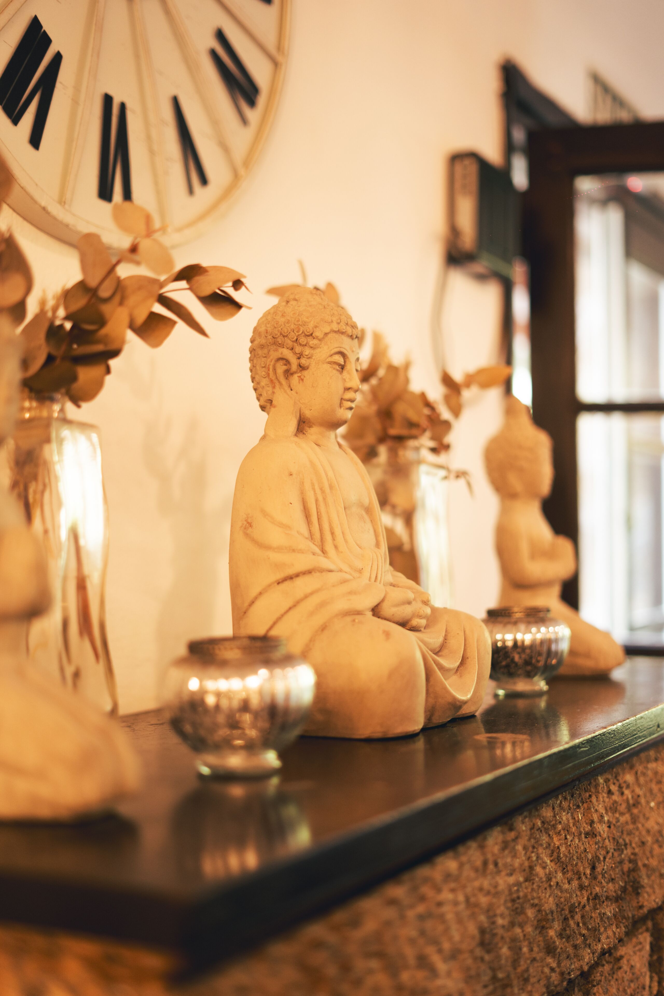 A Buddha statue on a shelf with a clock in the background.