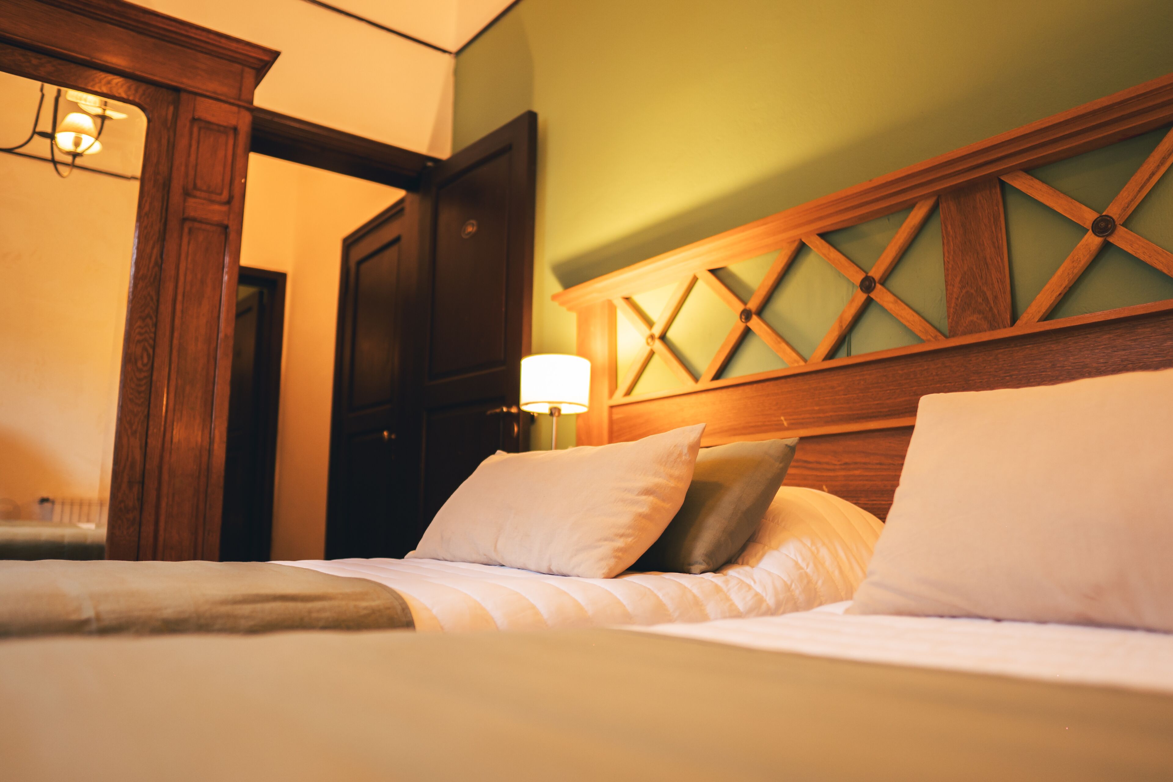 A neatly made bed with white linens and pillows, a wooden headboard with a geometric pattern, and a wall-mounted lamp.
