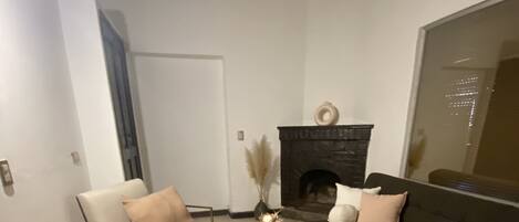 A modern living room with a dark-colored sofa, a white armchair, and a round coffee table. There is a fireplace with a decorative item on top.
