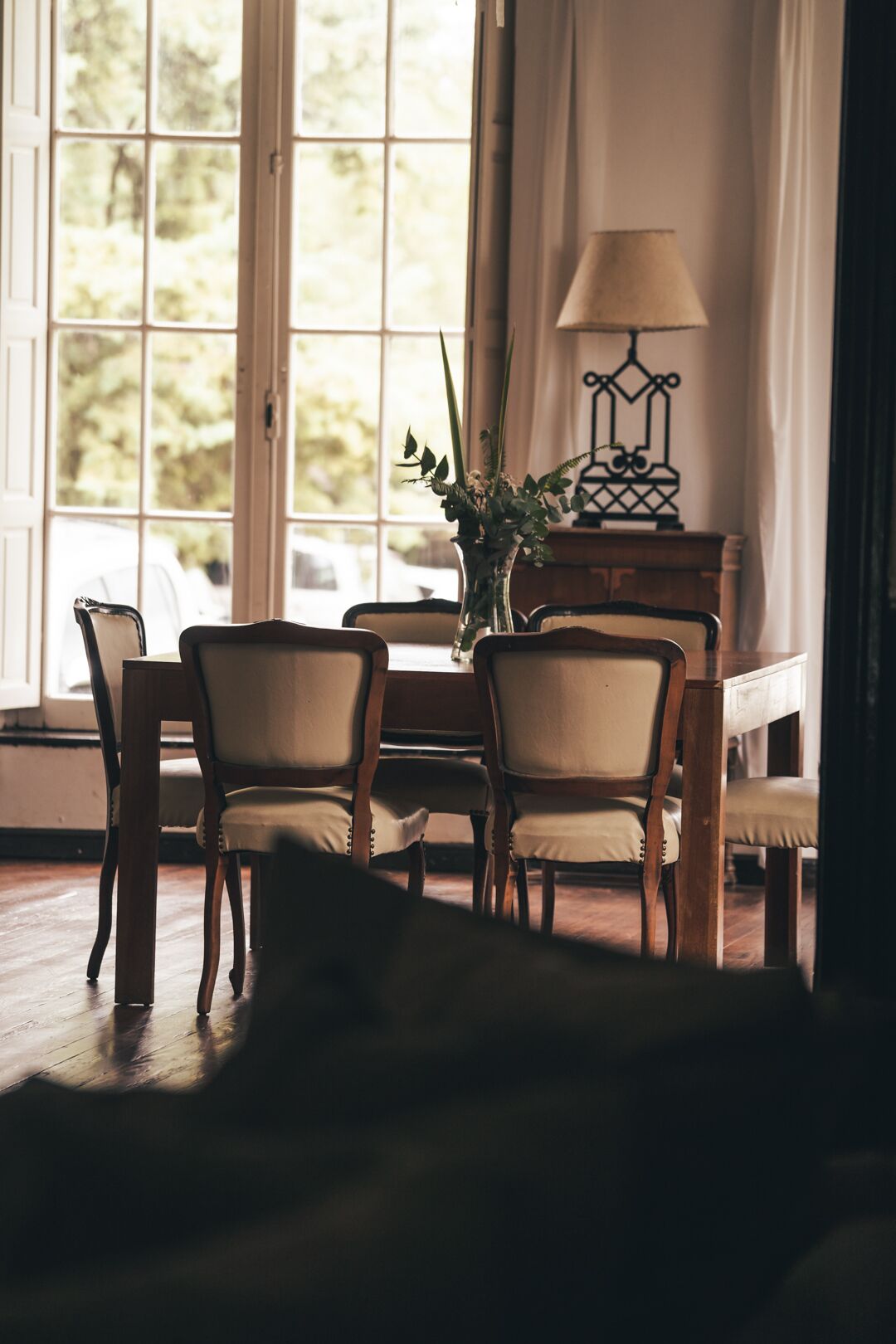 A dining area with a wooden table and chairs, a vase with flowers, and a lamp.