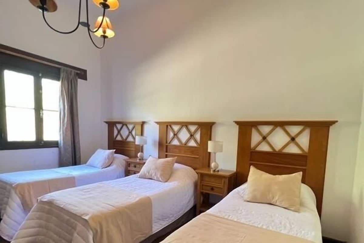 A hotel room with two single beds, wooden headboards, bedside tables with lamps, and a hanging light fixture.