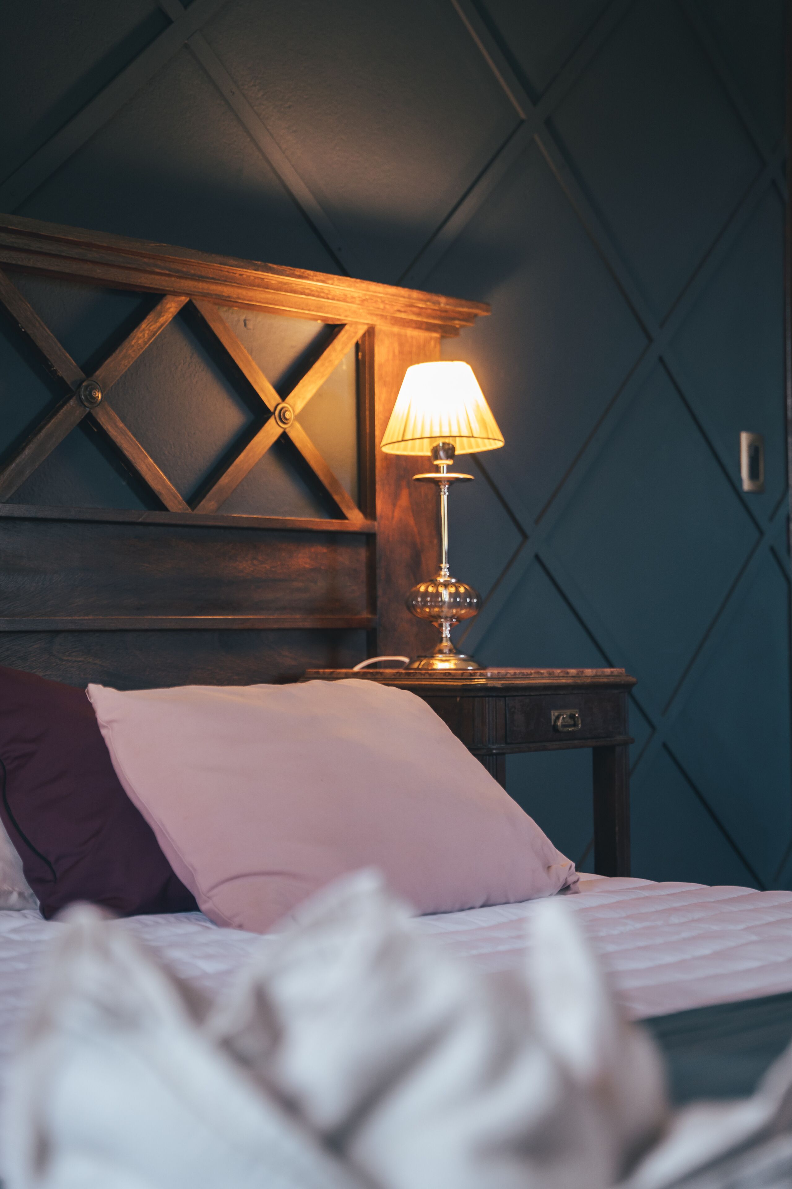 A bedroom with a bed, a nightstand, a lamp, and a wooden headboard.