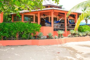 A building with a red exterior, multiple windows, and a covered outdoor seating area with a hammock. - Spooky Channel Villa (Roatan)