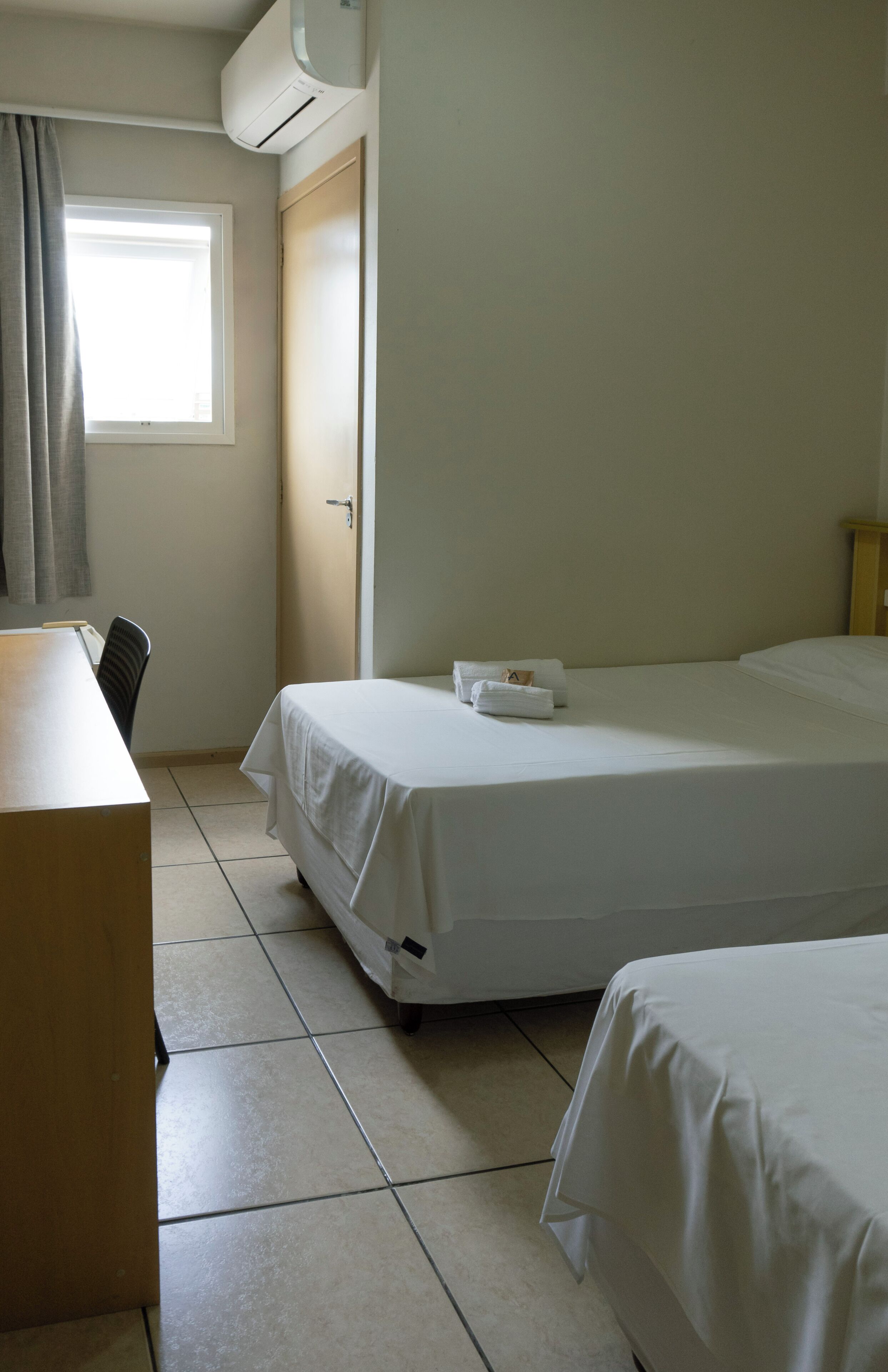 A hotel room with a bed, a desk, and a window with curtains.