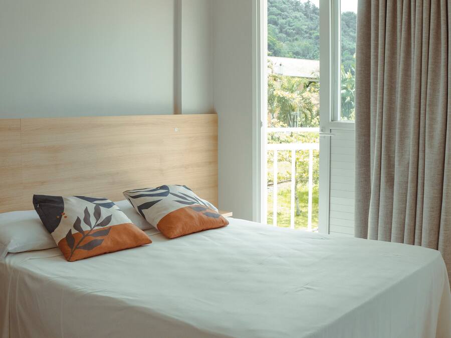 A bedroom with a bed, two pillows, a window, and a balcony.