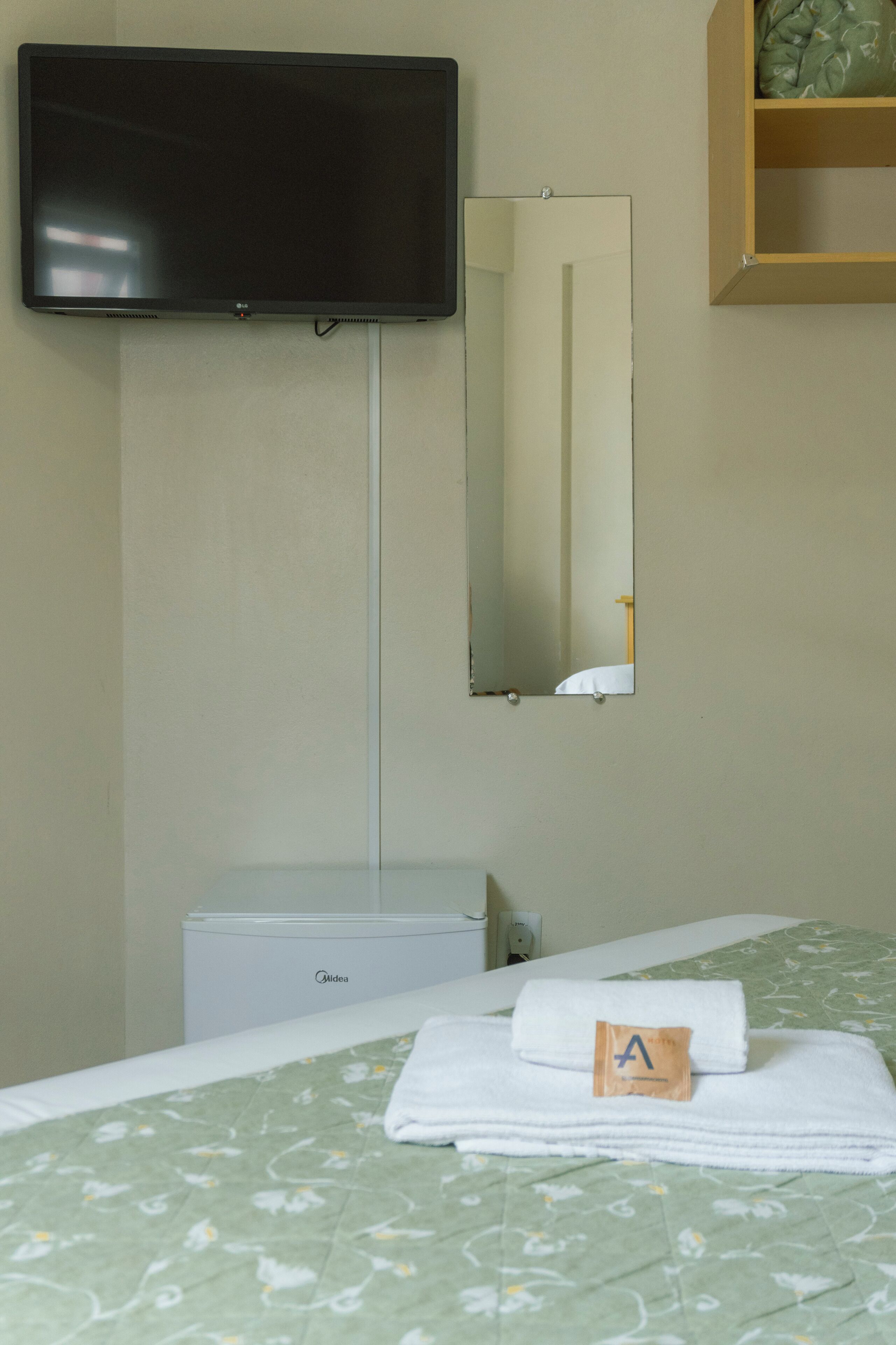 Een hotelkamer met een bed, een aan de muur bevestigde televisie, een spiegel en een klein wit kastje.