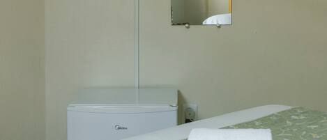 Habitación de hotel con cama, televisor montado en la pared, espejo y un pequeño armario blanco.