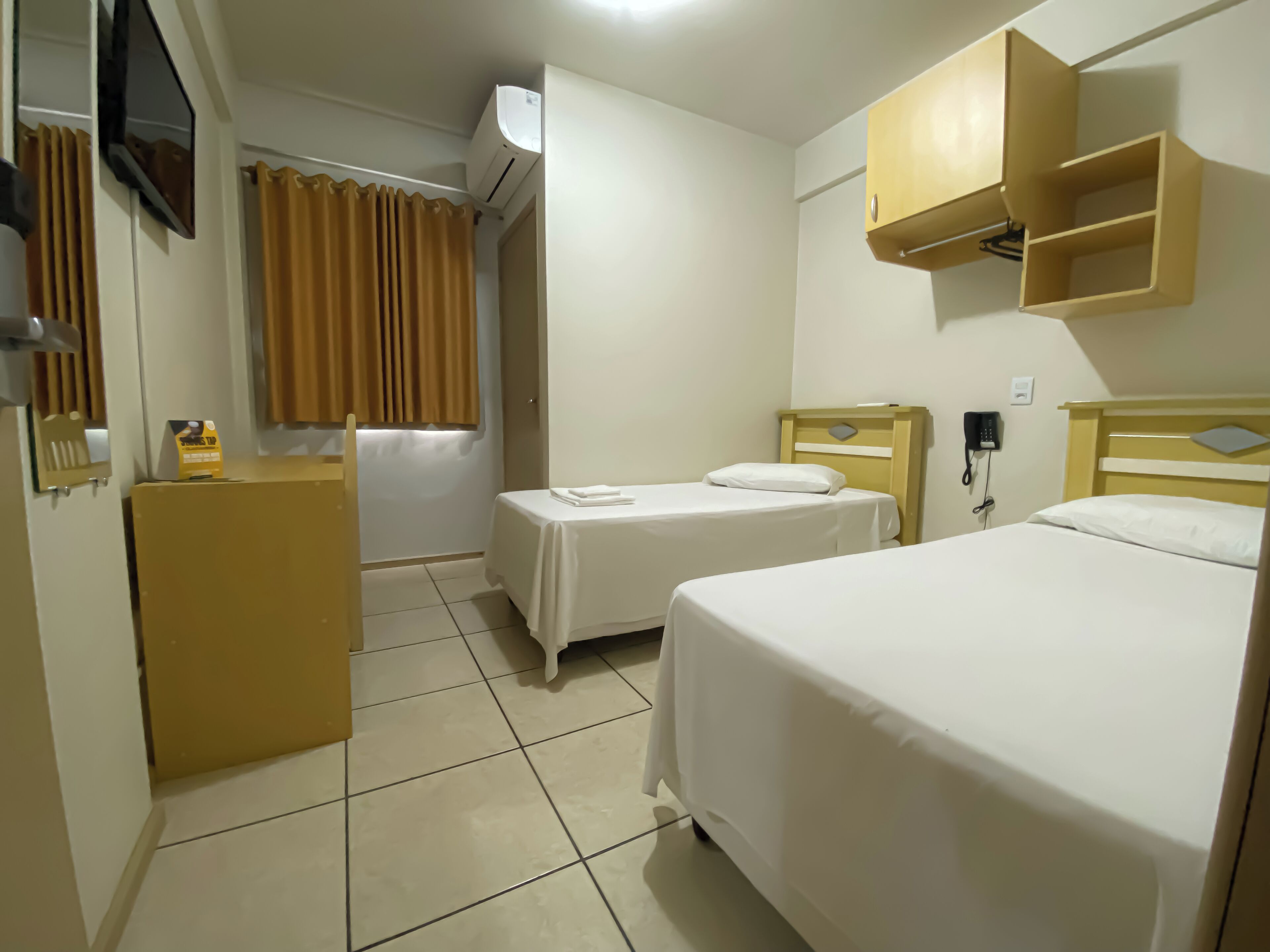 A hotel room with two single beds, a desk with a chair, a TV mounted on the wall, and a telephone.