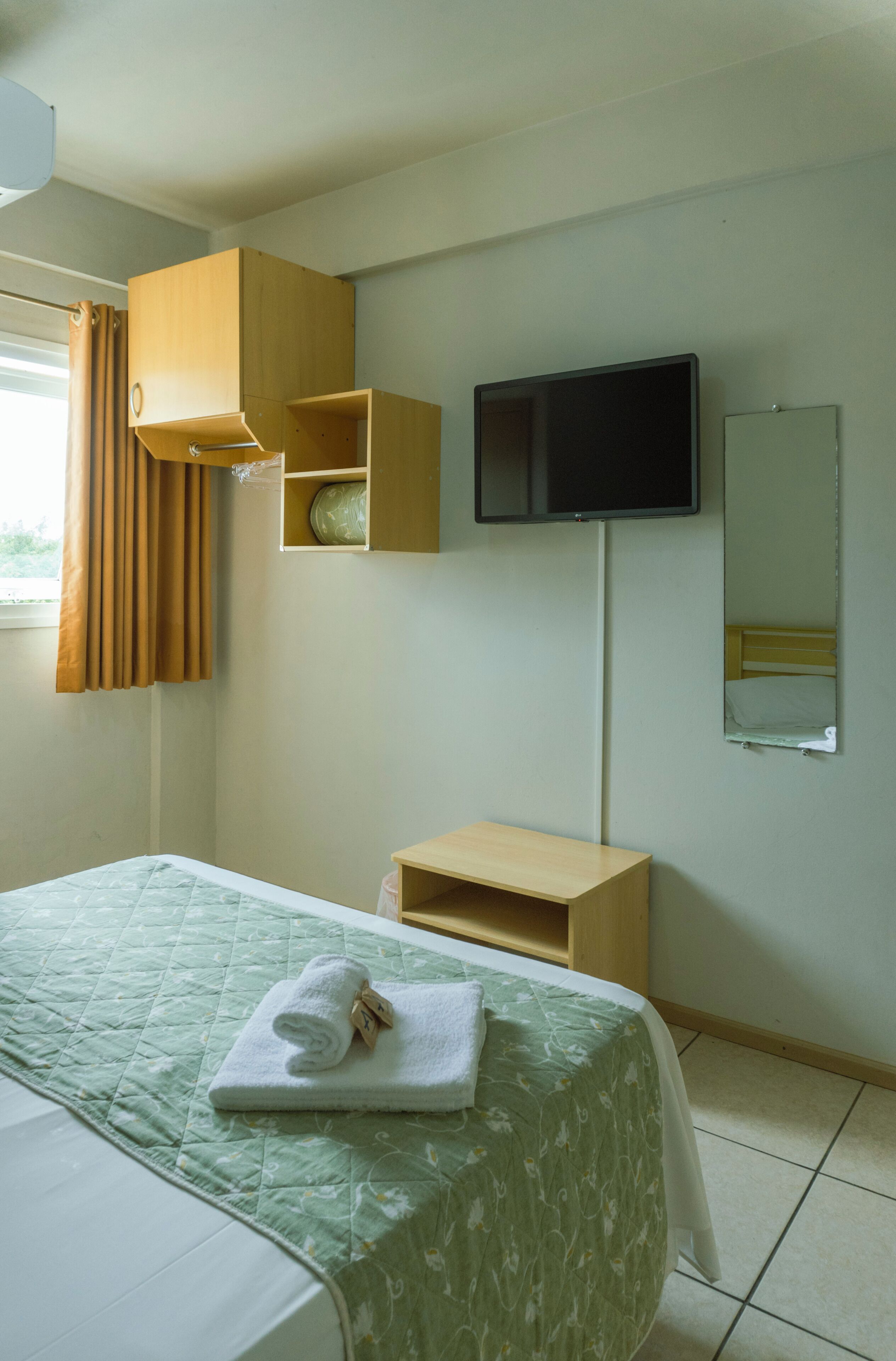 Una habitación de hotel con cama, televisión, espejo y armario de madera.