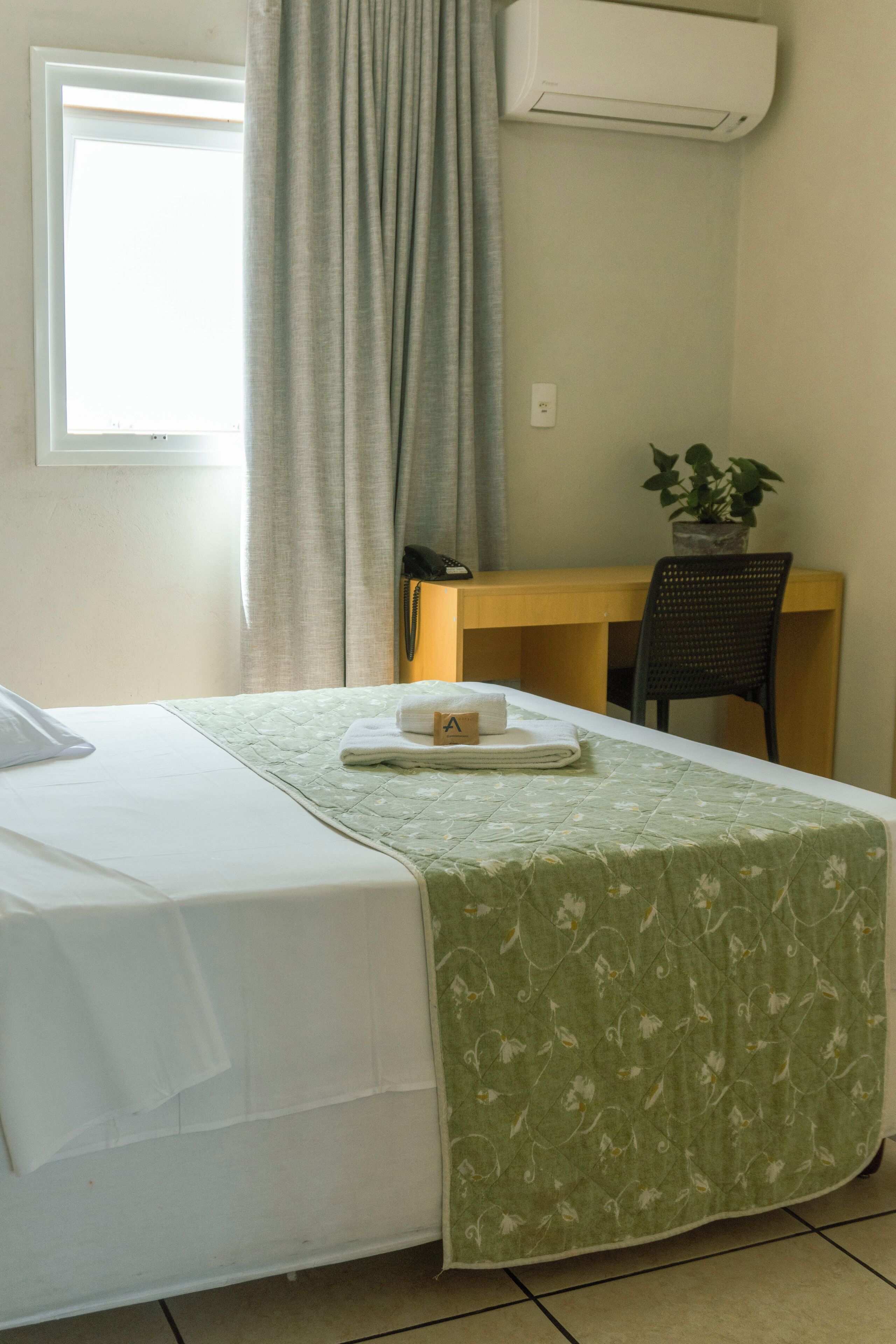 A hotel room with a bed, a desk, a chair, and a potted plant.