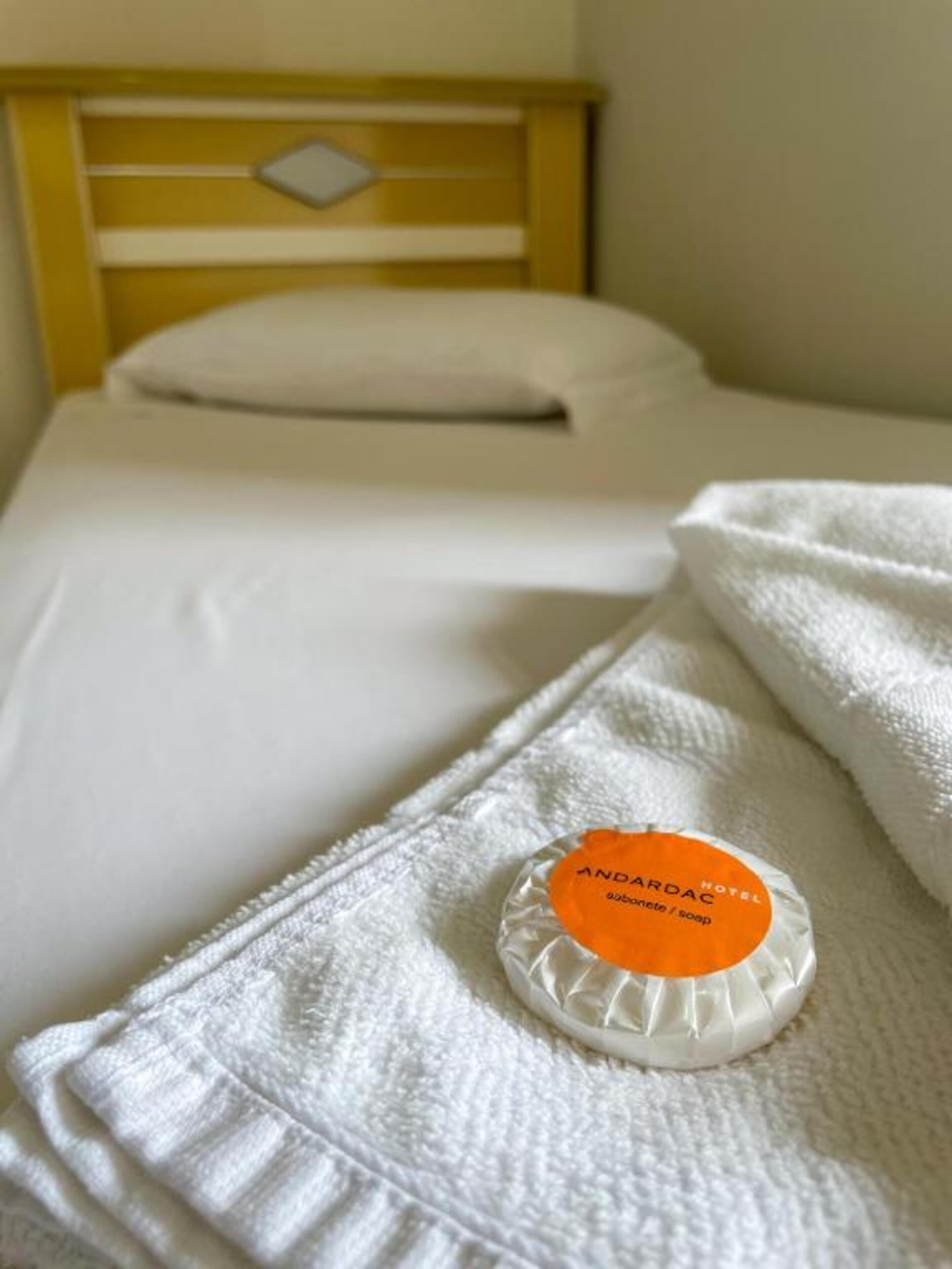 A bed with a white pillow and a white blanket. There is a white towel folded on the bed.