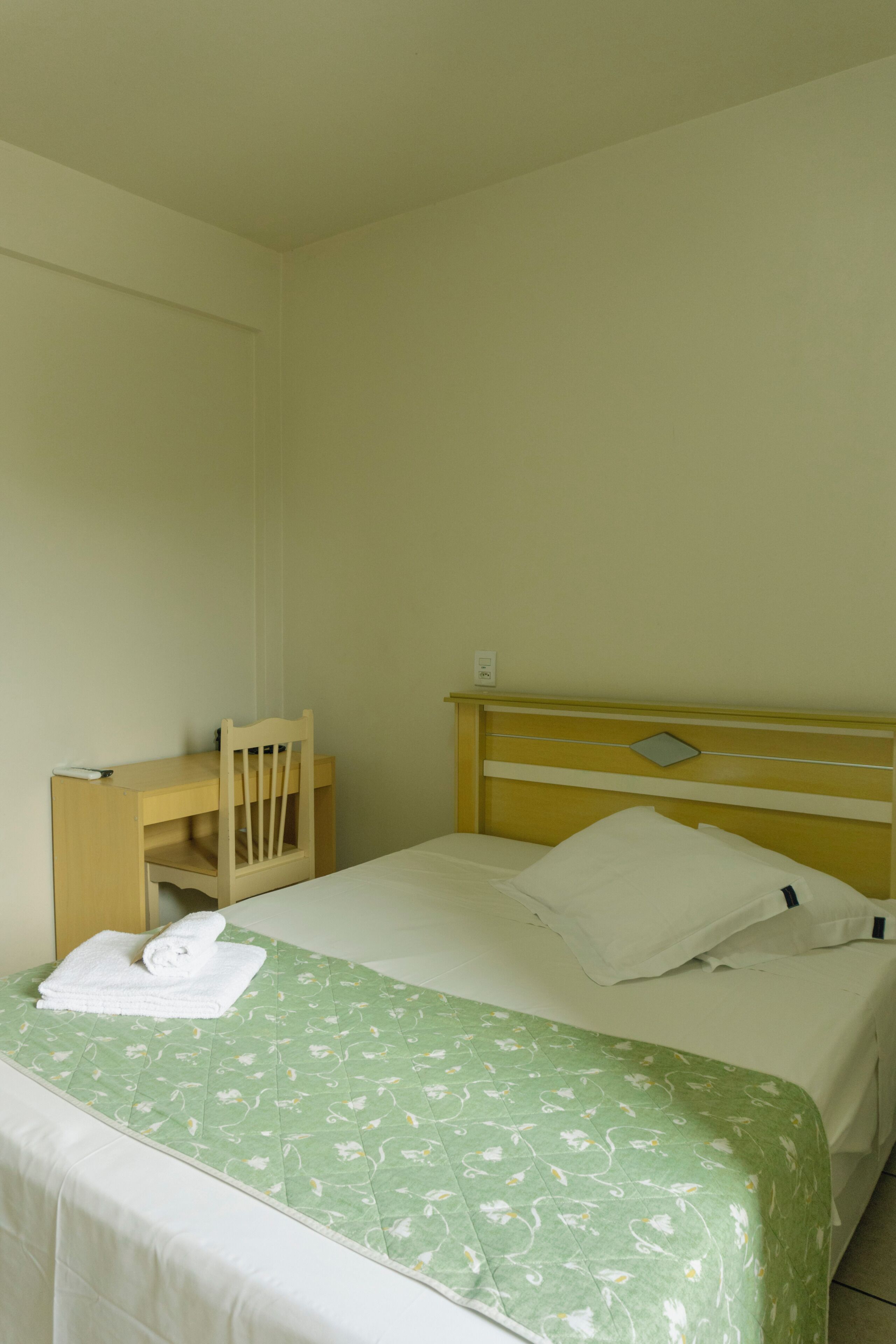 A simple, clean room with a bed, a desk, and a chair.