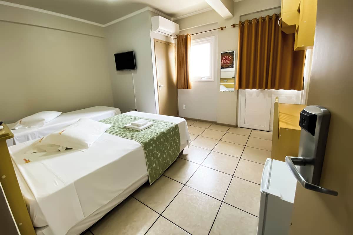 A hotel room with two beds, a flat-screen TV, a window with curtains, a door, and a thermostat.