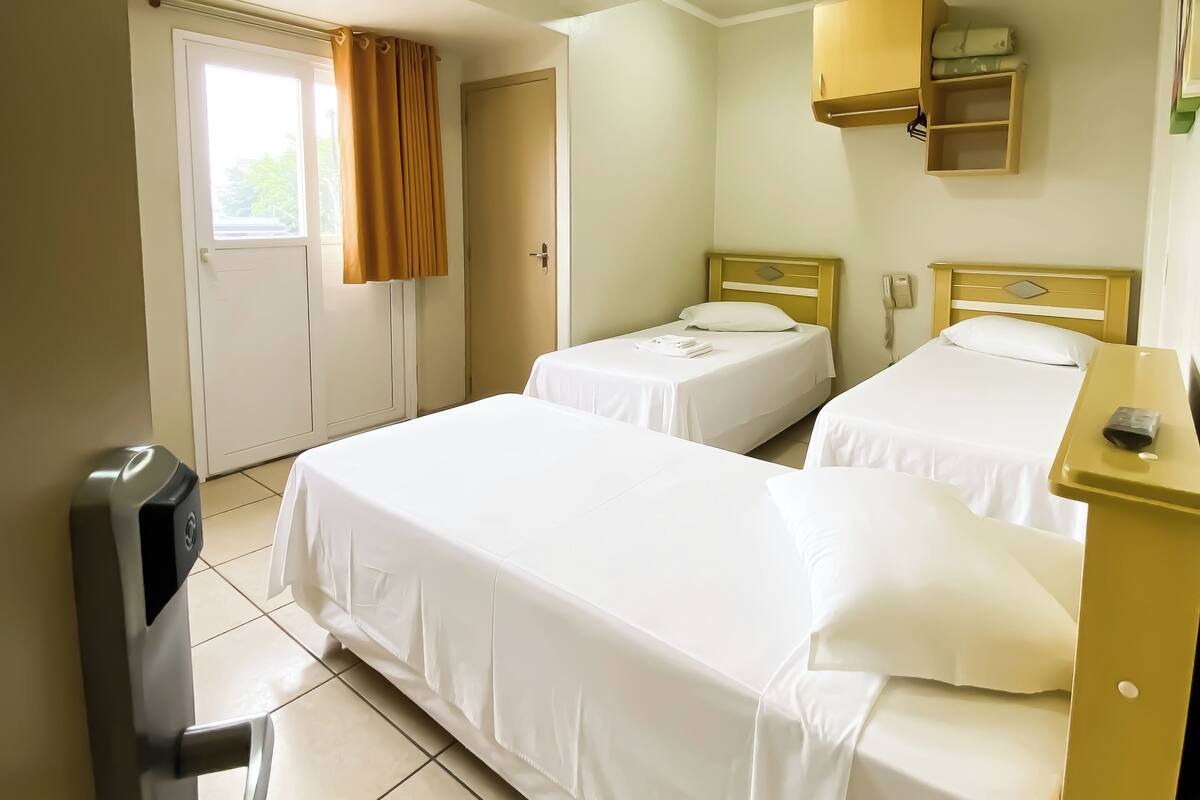 A hotel room with two single beds, a desk with a telephone, a cabinet above the bed, and a door with a curtain.