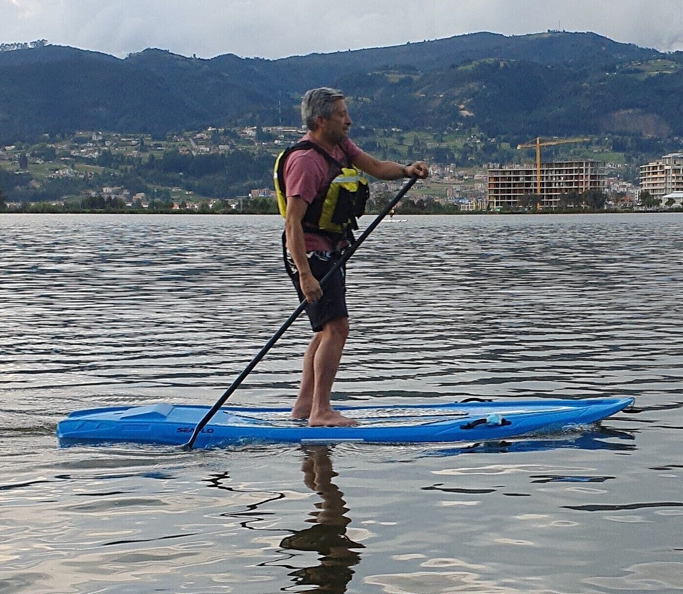 Una persona practicando paddleboard en aguas tranquilas, con montañas al fondo.
