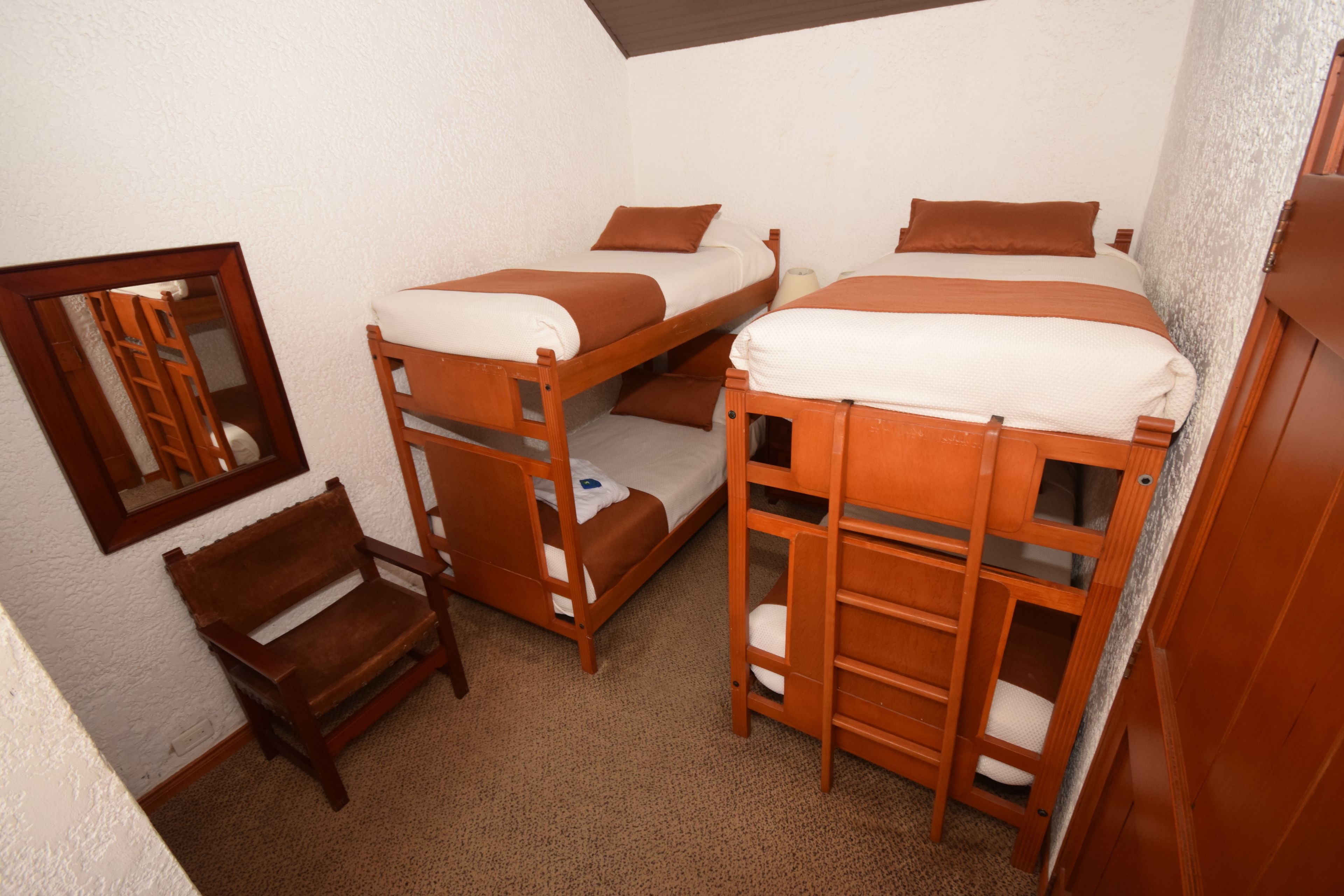 A compact room with bunk beds, a wooden chair, and a mirror on the wall.