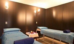 Ein Zimmer mit zwei Betten, jeweils mit blauer Bettdecke und Kissen, sowie einem kleinen Tisch mit Kerze und Blumen.