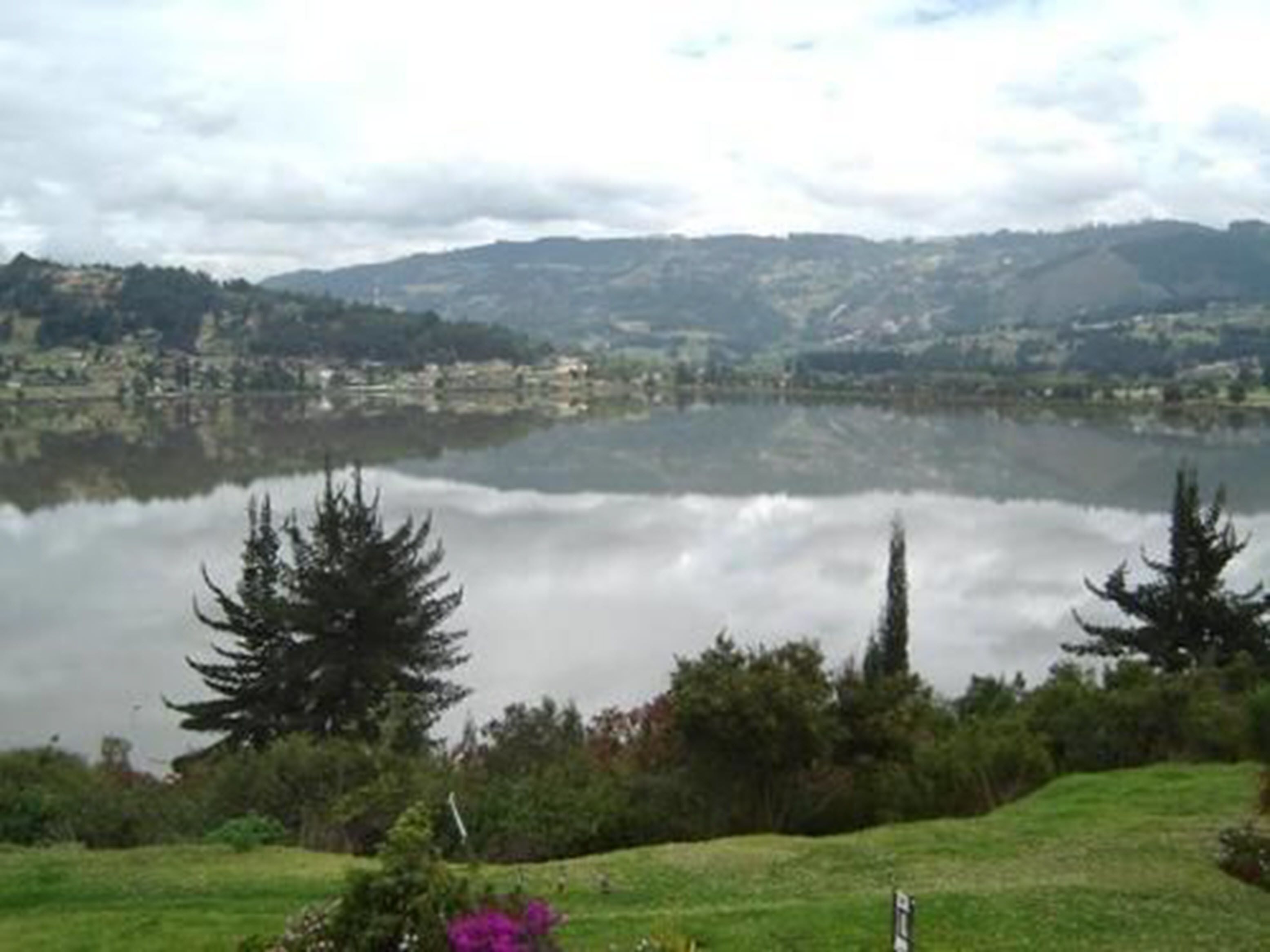 A lake with surrounding greenery and hills in the background.