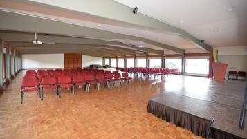 A large hall with rows of red chairs and a stage.
