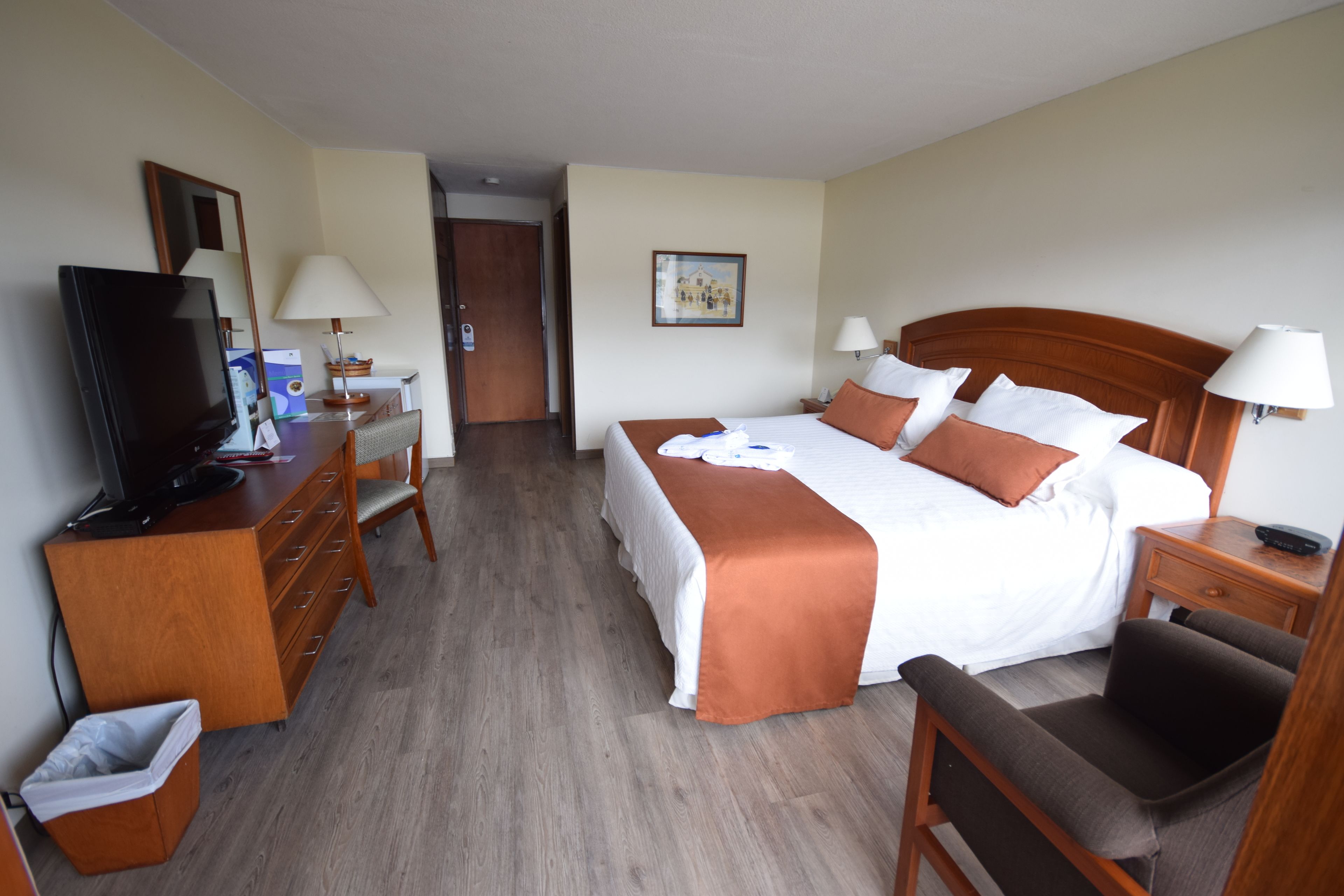 Een hotelkamer met een bed, een bureau met televisie, een stoel, een nachtkastje en een lamp.