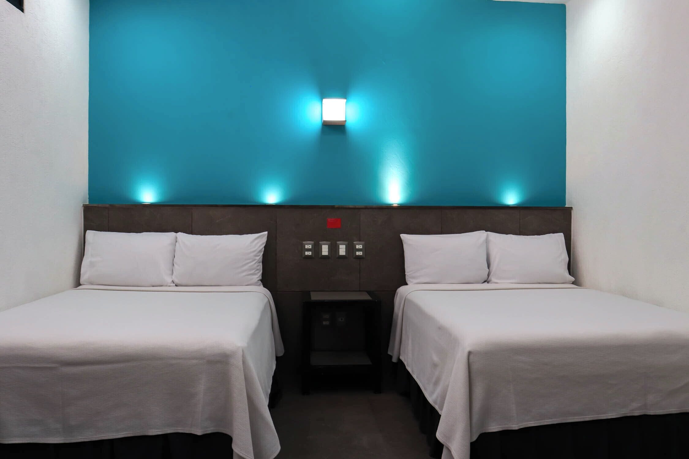 Ett hotellrum med två separata sängar, ett nattduksbord, en väggmonterad lampa och en röd varningslampa.