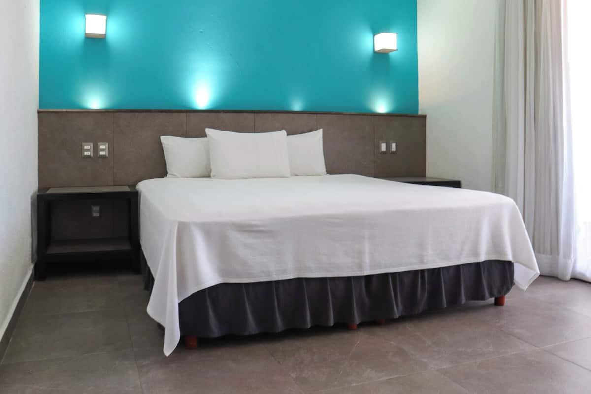 A hotel room with a large bed, two bedside tables, a teal accent wall, and a window with curtains.