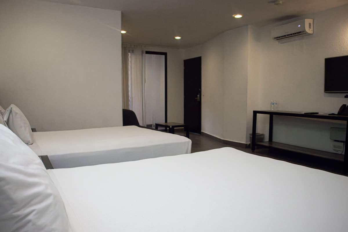 A hotel room with two beds, a desk, a chair, an air conditioning unit, and a television on the wall.