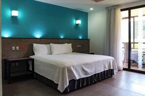Une chambre d’hôtel avec un grand lit, deux tables de chevet, un mur d’accent de couleur turquoise et une porte-fenêtre coulissante donnant sur le balcon.