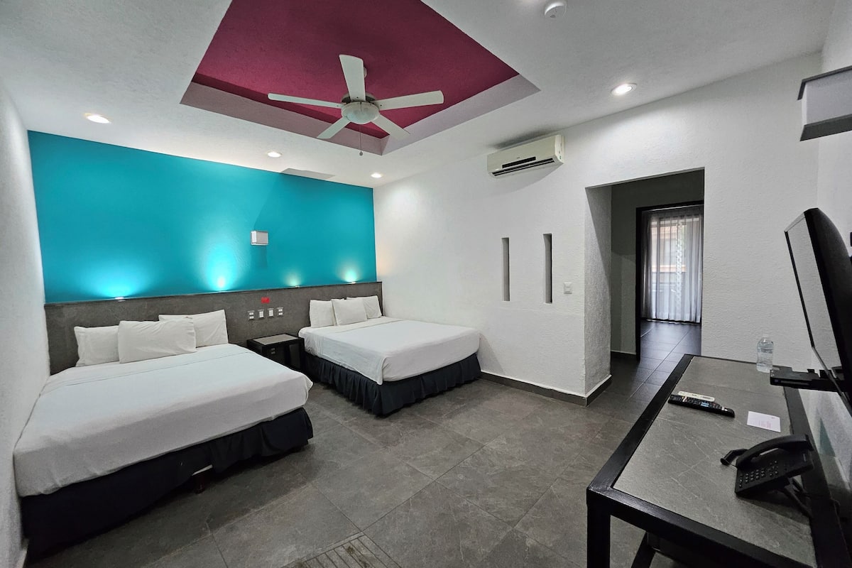 A hotel room with two beds, a desk, a chair, a ceiling fan, recessed lighting, and an air conditioning unit.
