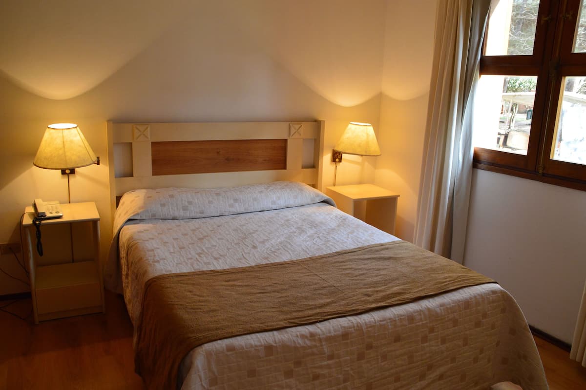 A neatly made bed with a wooden headboard, two bedside lamps, and a window with curtains.