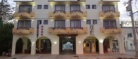 A hotel with a central entrance, multiple balconies, and a sign indicating it is a hotel.