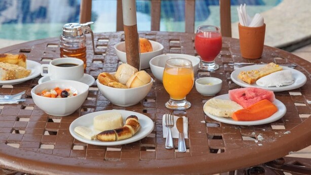 A dining table with breakfast items and drinks by a poolside. - Ritz Plazamar Hotel (Maceió)