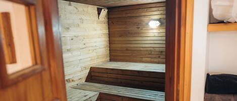 A sauna room with wooden benches and a bench in the center. There is a wooden door leading to the room.