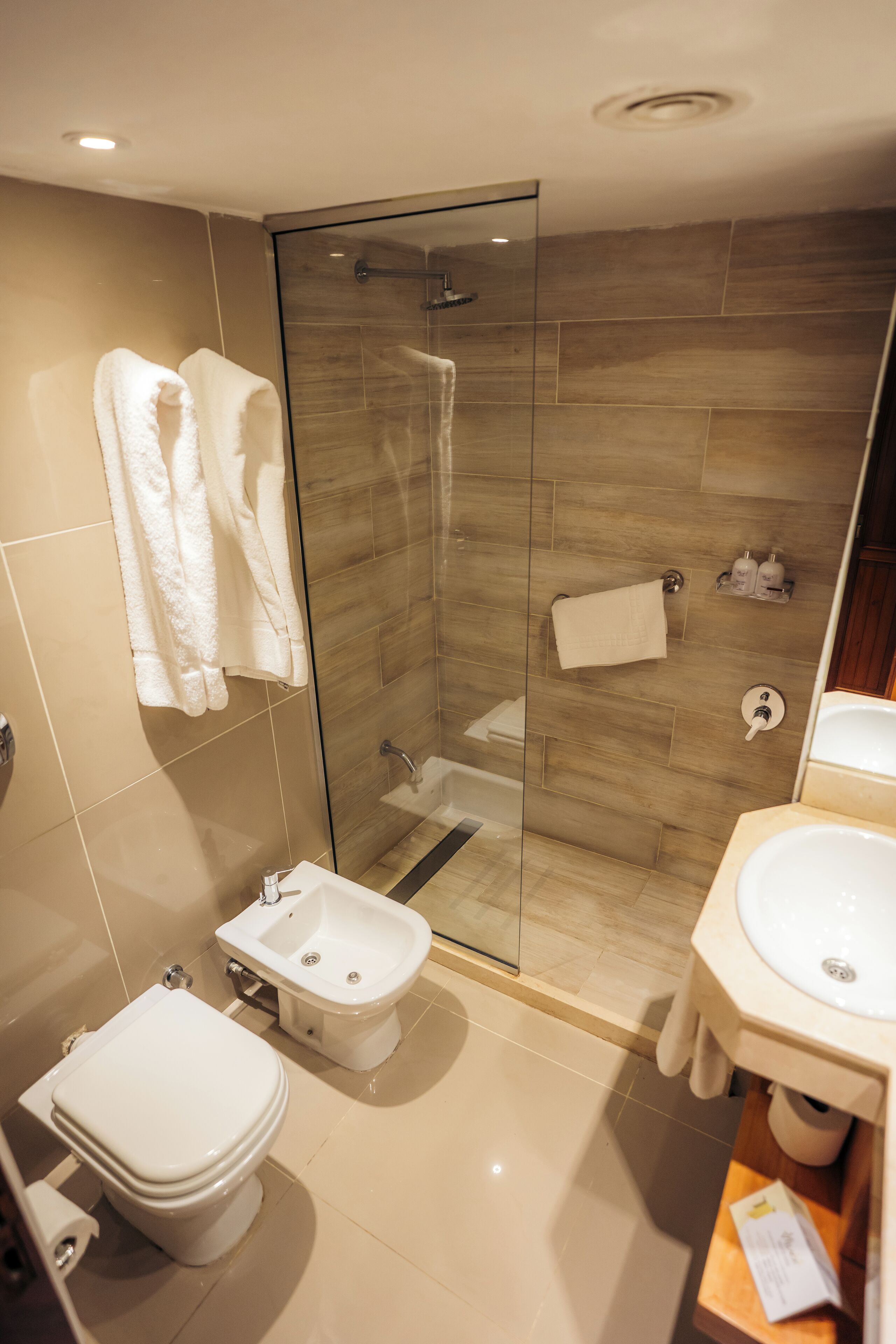 A modern bathroom with a glass-enclosed shower, a bidet, a toilet, and a sink.