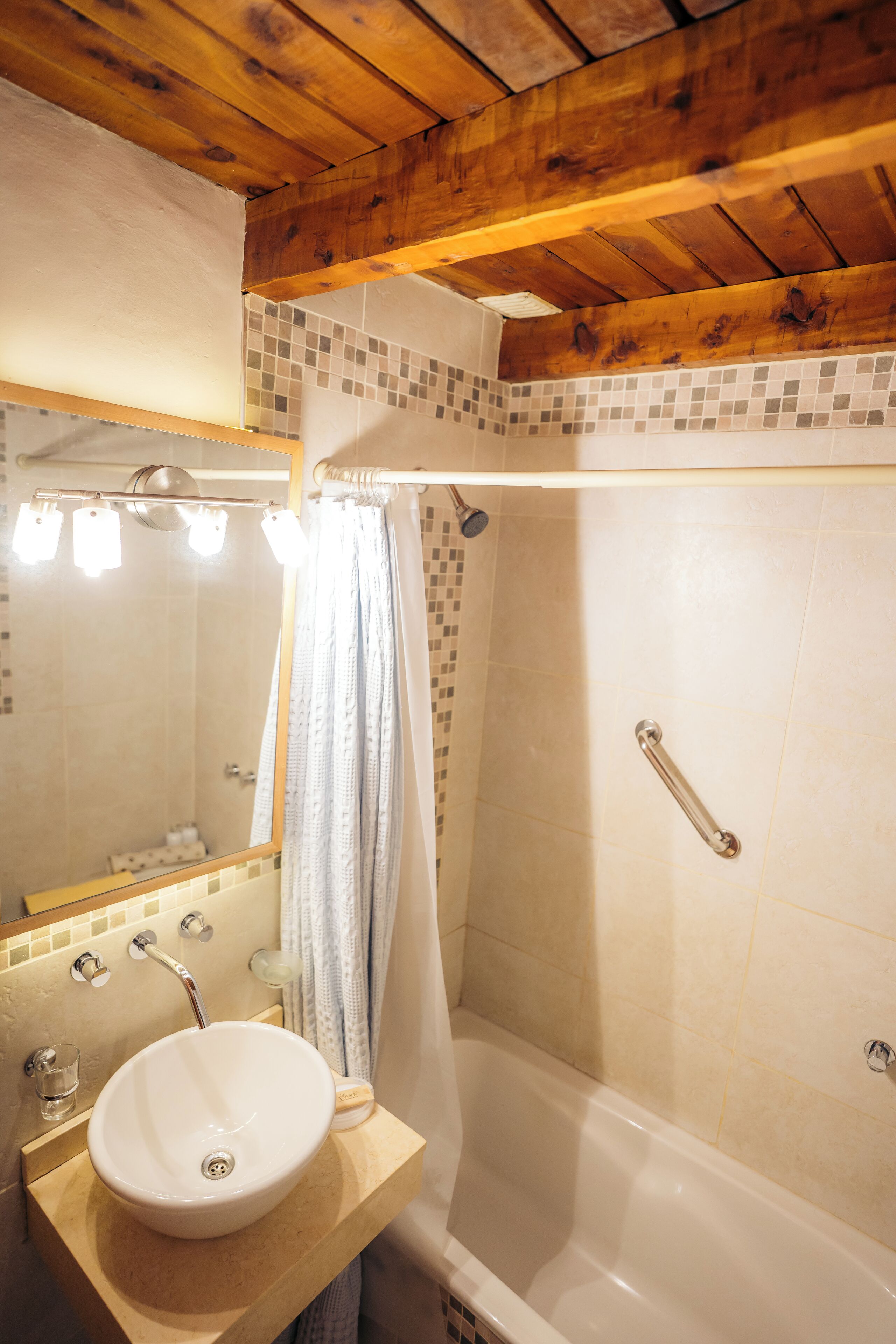 Un bany amb sostre de fusta, un lavabo blanc, una banyera i una dutxa amb cortina.