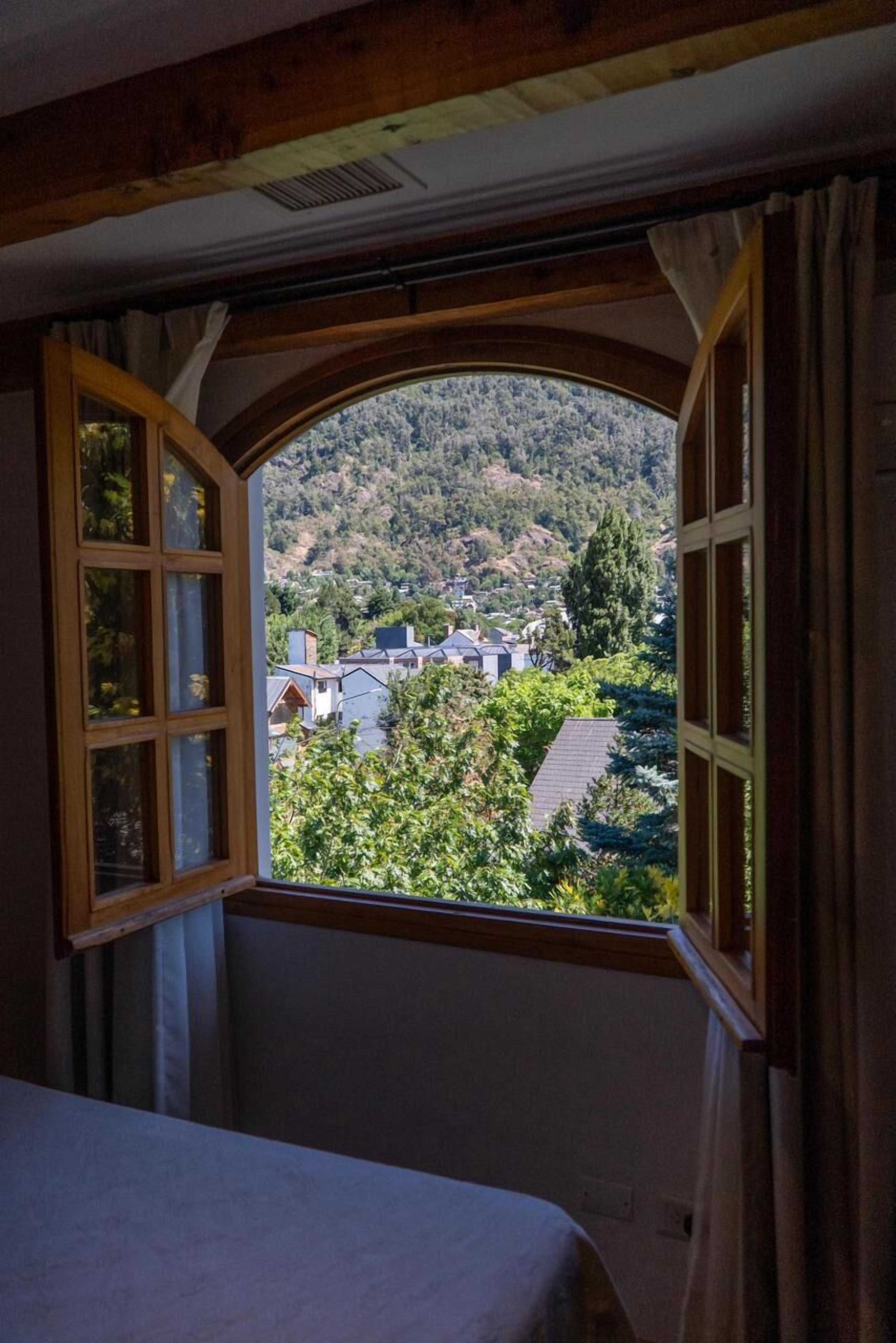 Quarto com uma grande janela em arco que oferece vista para uma vila no topo do morro.