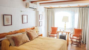 A hotel room with a large bed, wooden beams, a small table with chairs, and a window with curtains.