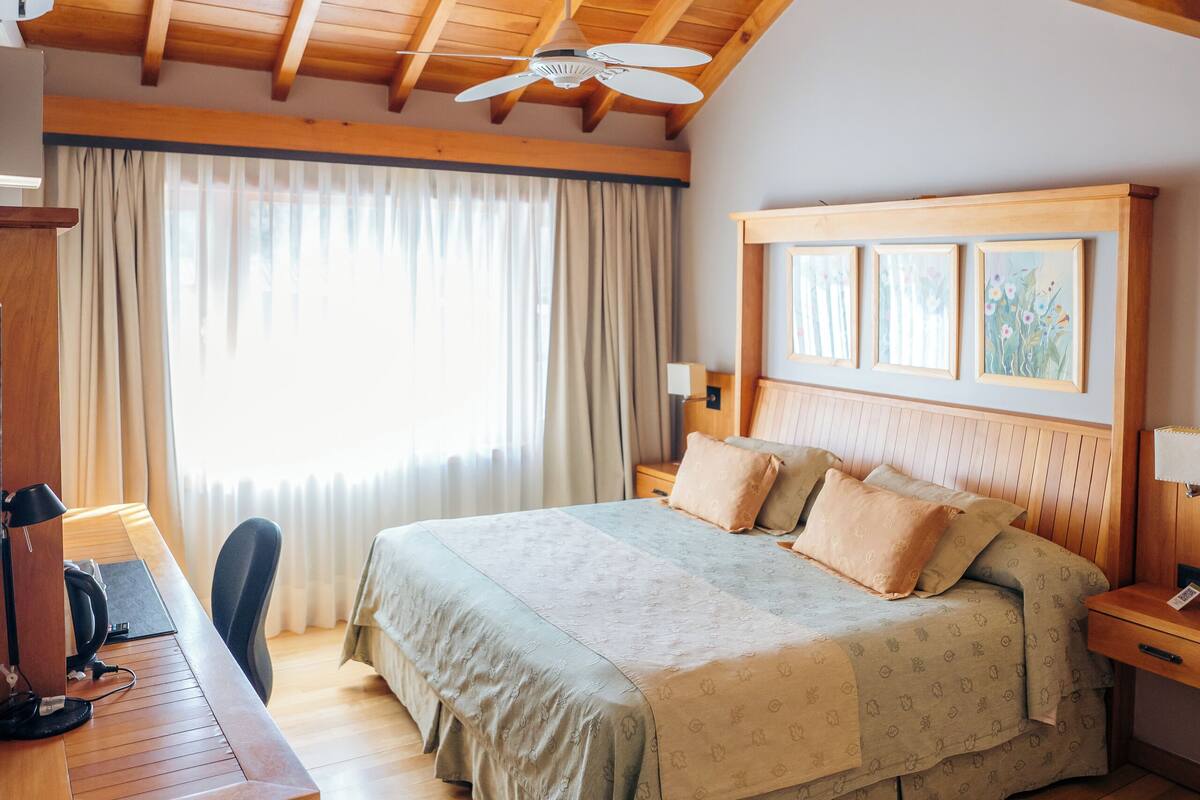 A wooden-paneled bedroom with a bed, desk, and ceiling fan.
