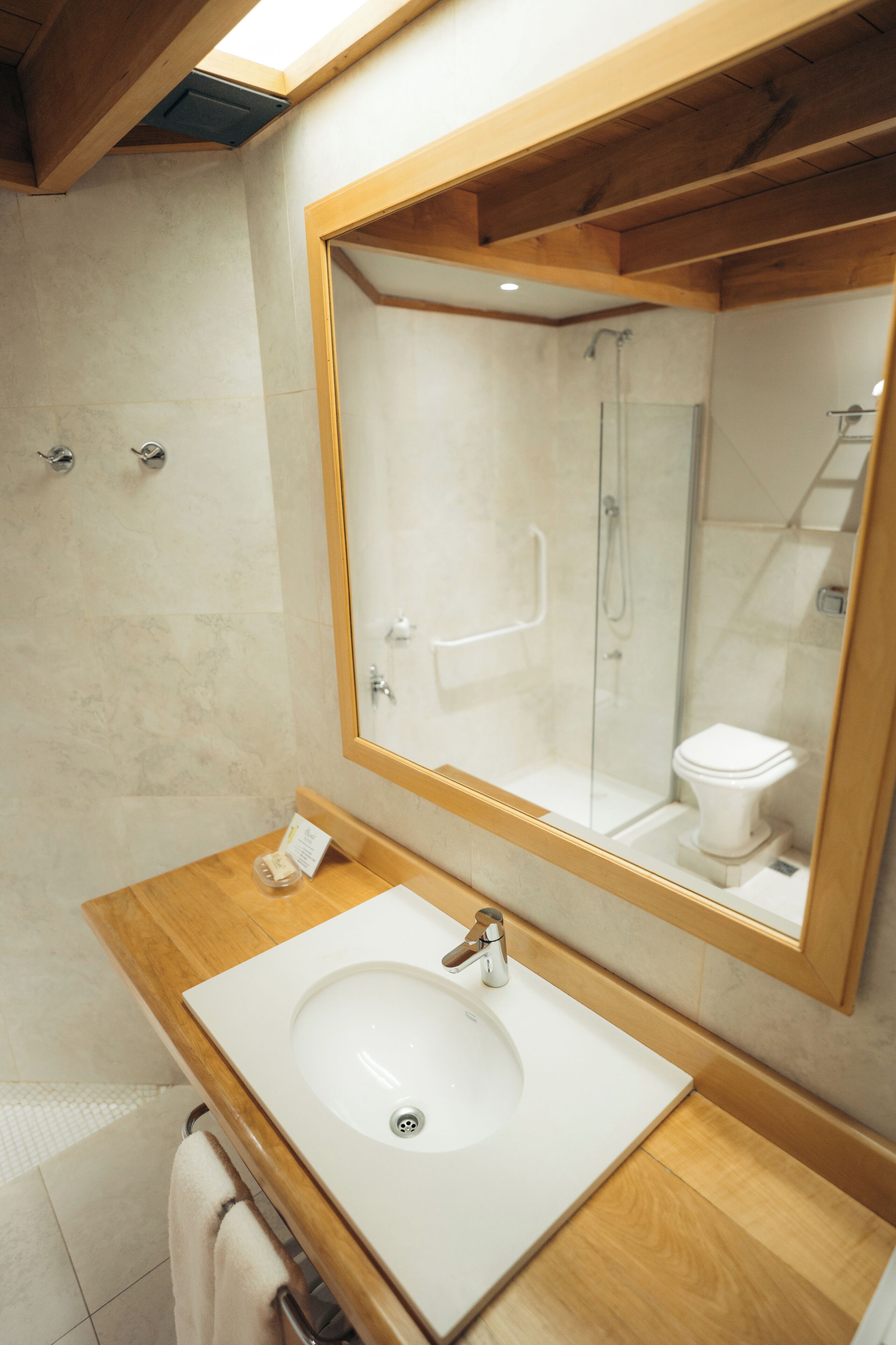 A modern bathroom with a large mirror, a wooden vanity, a white sink, and a glass-enclosed shower.