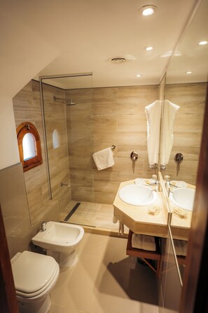 Un baño moderno con ducha de mampara de vidrio, dos lavamanos, un bidé y una ventana pequeña.