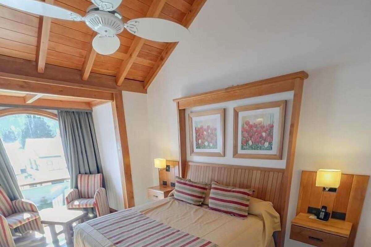A bedroom with a bed, two bedside tables, a ceiling fan, and a window with curtains.