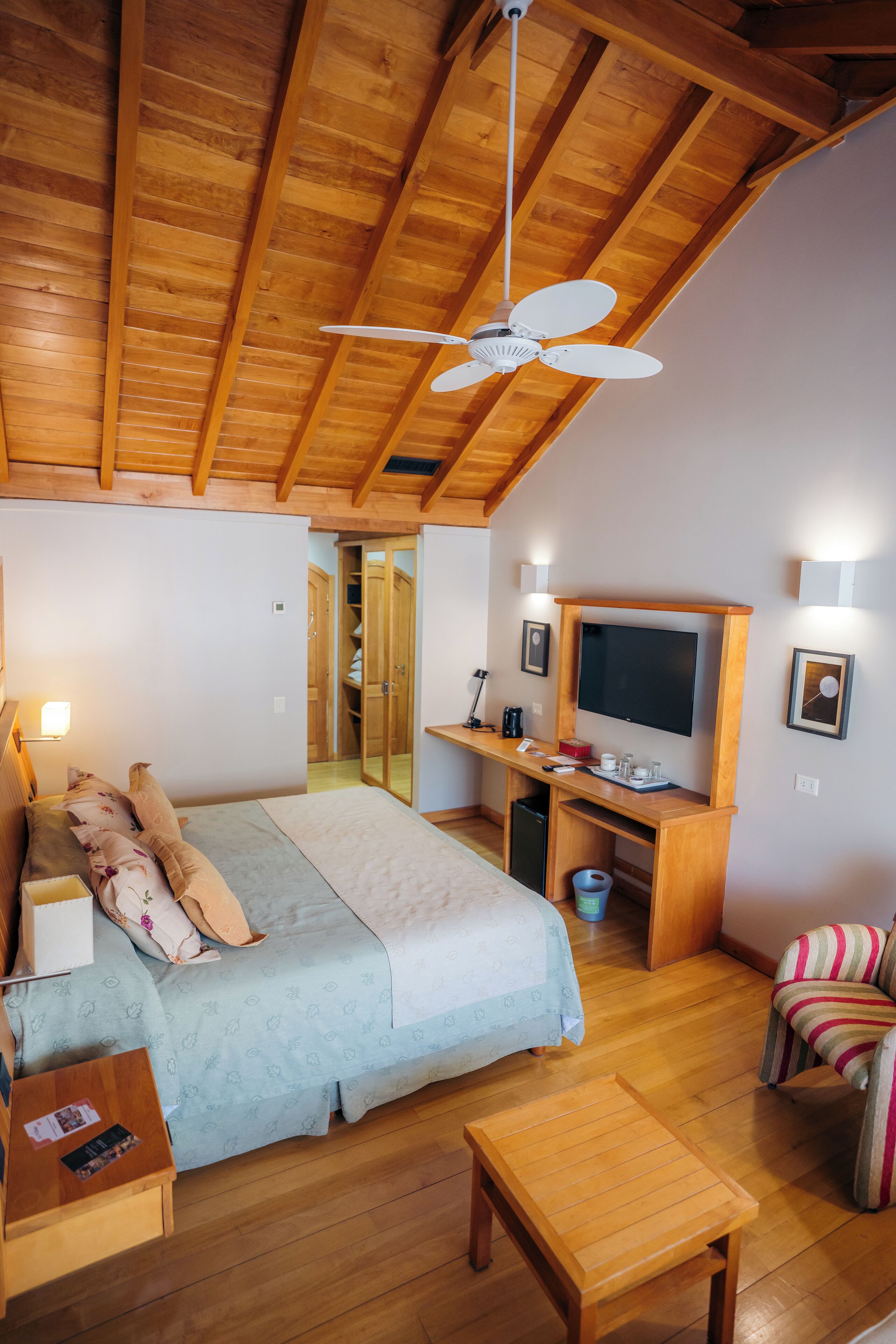 Une chambre à coucher comprenant un lit, une table de chevet, un bureau en bois, une télévision et un ventilateur de plafond.