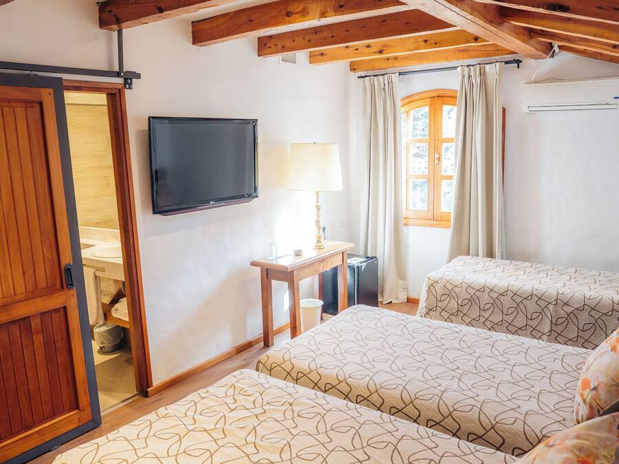 A bedroom with two beds, wooden beams, a TV, a desk, and a window with curtains.
