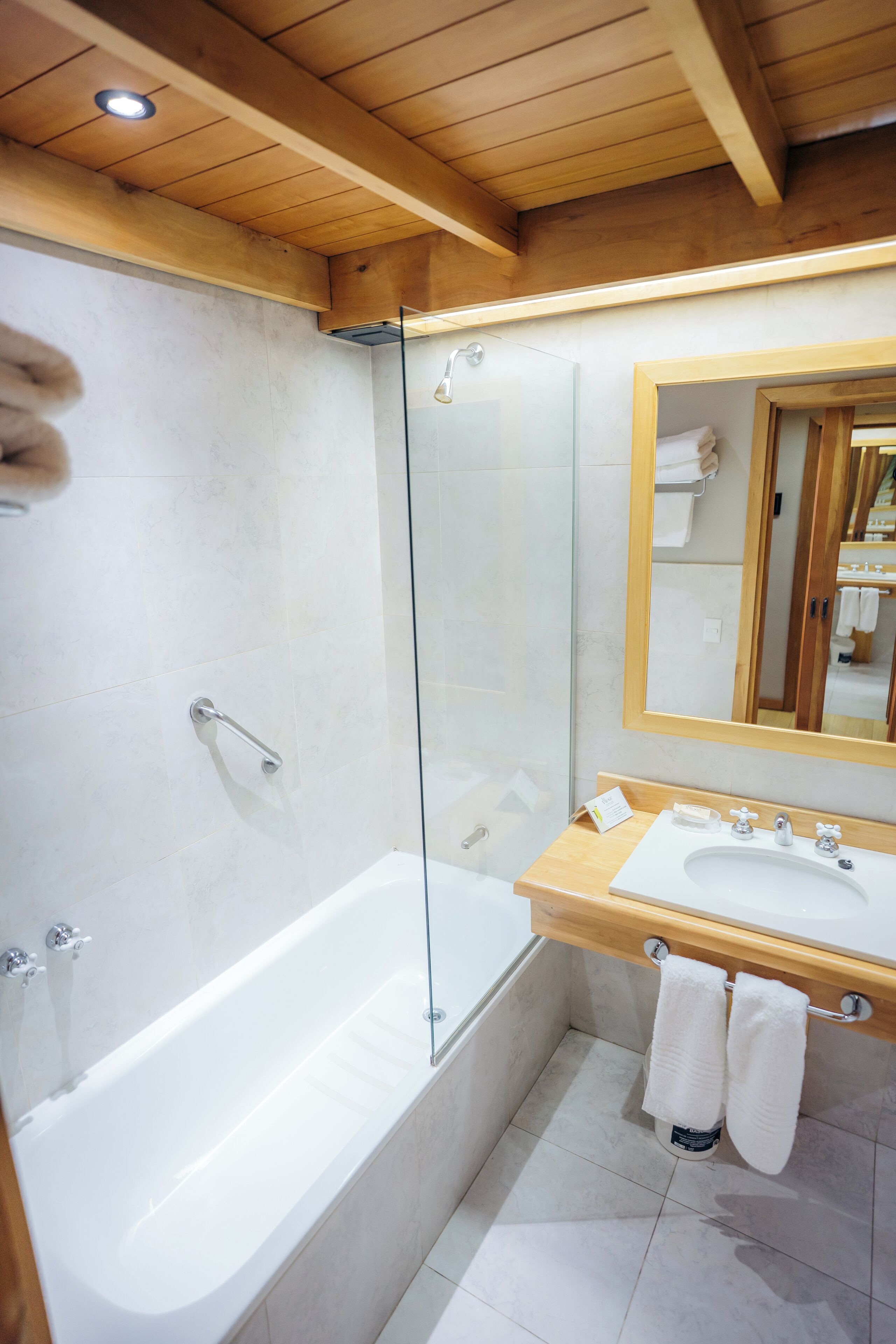 Une salle de bain moderne avec une douche à l’italienne en verre, un meuble-lavabo en bois et un grand miroir.