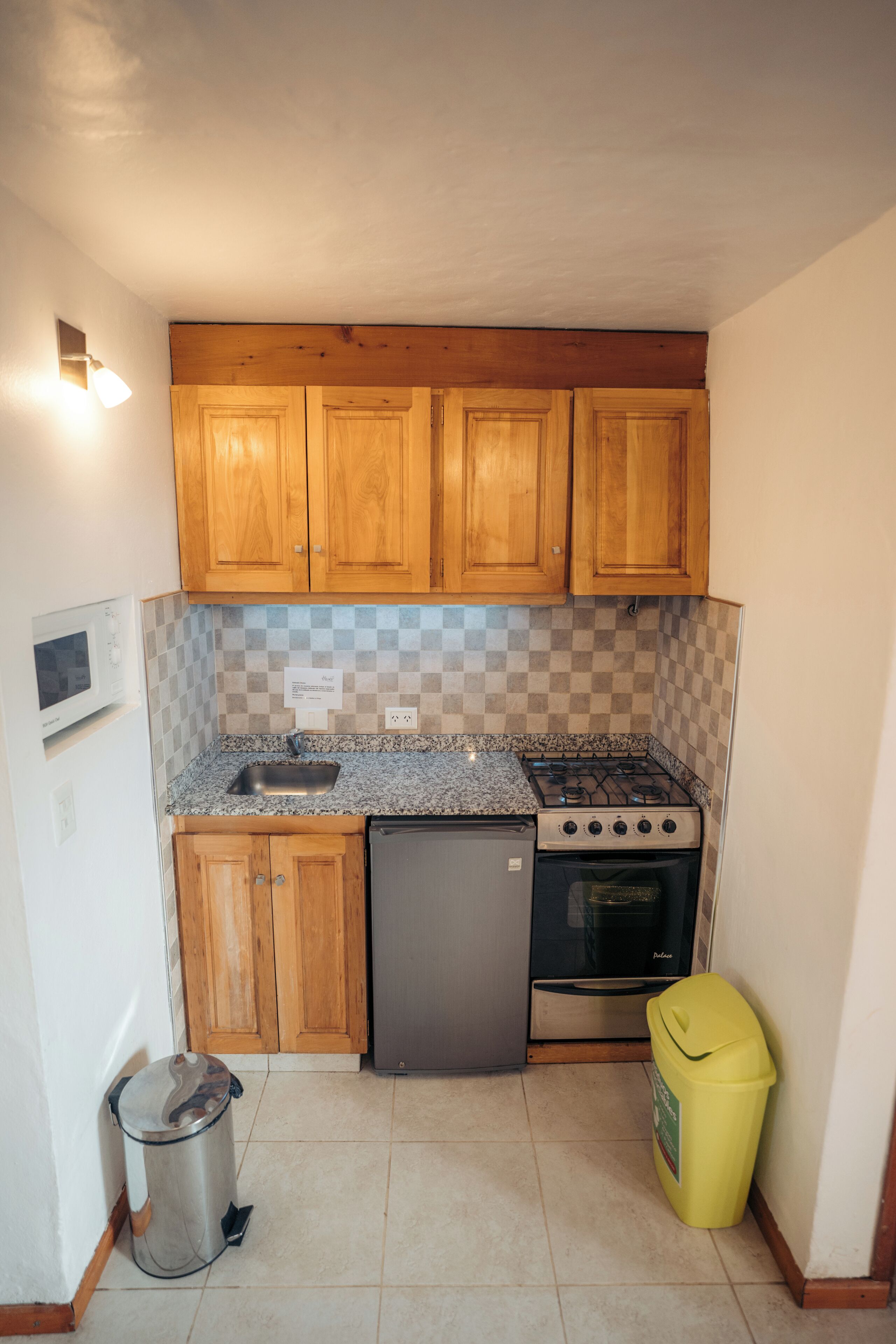 A compact kitchen with wooden cabinets, a gas stove, a built-in oven, a sink, a microwave, and a trash bin.
