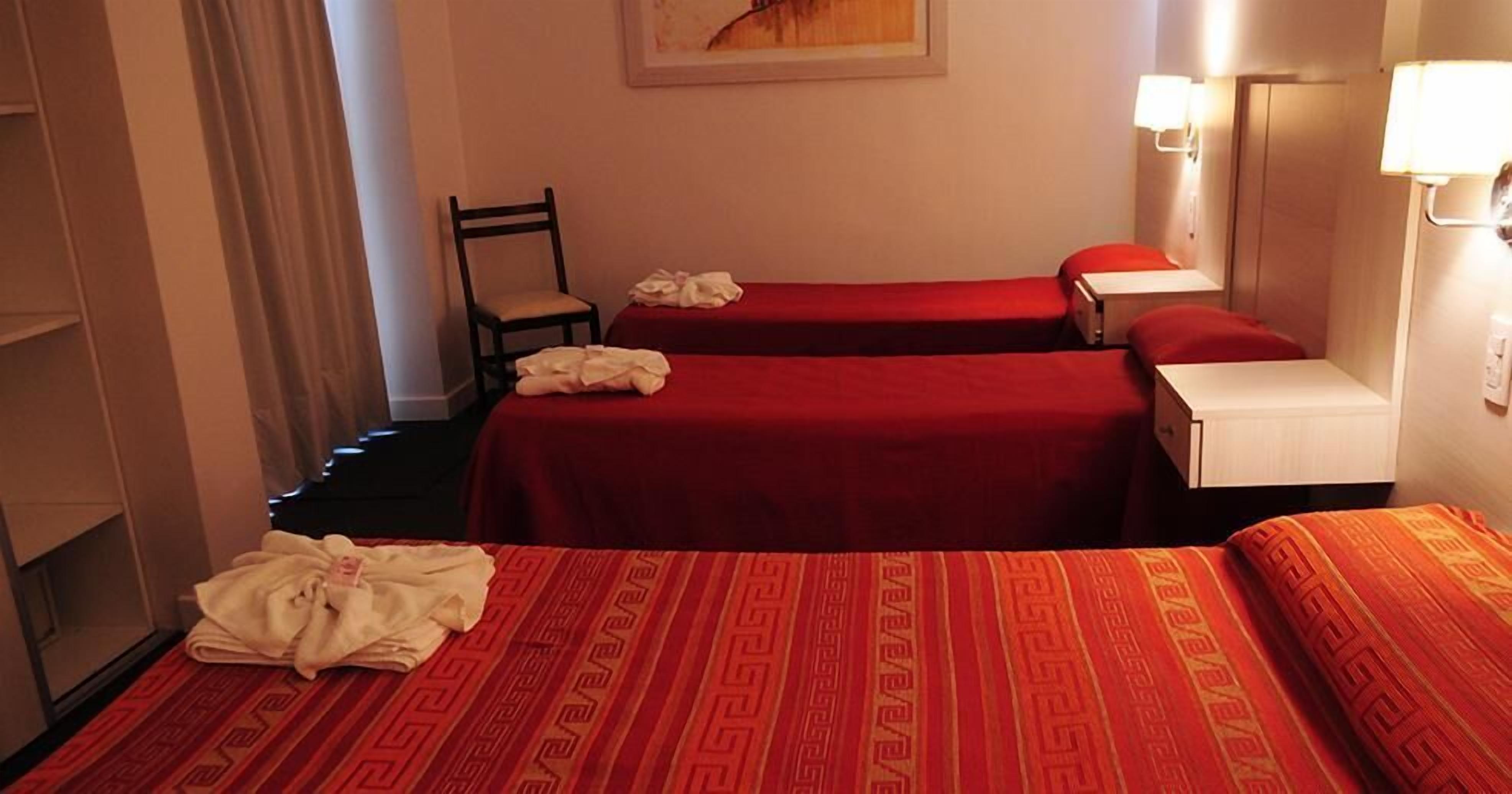 Une chambre d’hôtel avec deux lits, une chaise et une table de chevet avec une lampe.