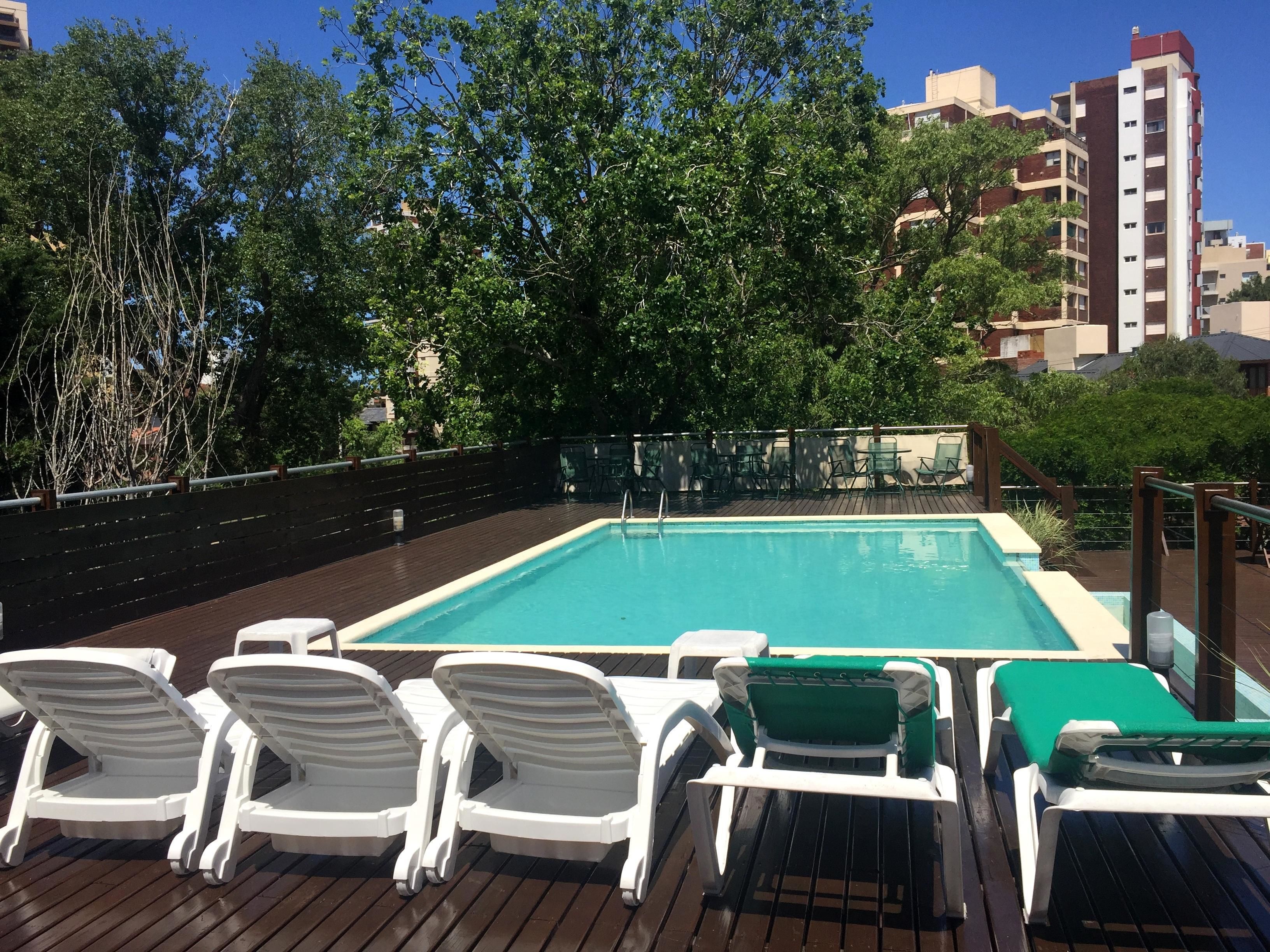 A rooftop pool with white and green lounge chairs, surrounded by trees and buildings.